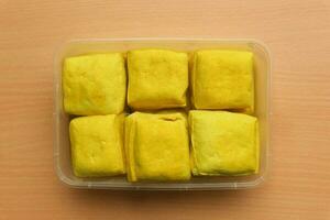 Tahu Kuning Cibuntu or Yellow tofu in the plastic container on the wooden background photo