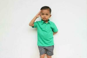 Portrait of a cute little Asian boy with a serious face doing the salute like a military while looking at the camera, isolated on the white background photo