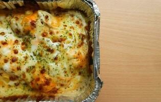 Pasta Makaroni Saus Keju or Pasta Mac and cheese in the aluminium foil bowl on the wooden background photo