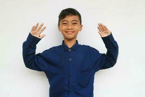 alegre pequeño chico en Rápido sonriente cara mientras elevado el manos, aislado en blanco antecedentes. un 10 años antiguo chico haciendo un gracioso rostro. foto