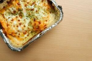 Pasta Makaroni Saus Keju or Pasta Mac and cheese in the aluminium foil bowl on the wooden background photo