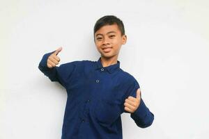 Smiling confident boy wearing a blue casual shirt looking at the camera with showing two thumb up isolated on white background photo