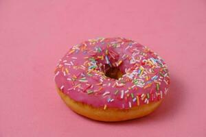 Donut with pink icing and multicolored sugar sprinkles.On pink background. photo