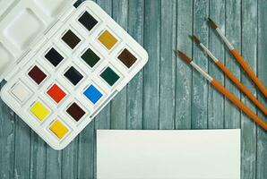 A set of new and unused watercolors, brushes and a piece of white paper on a textured surface ready to be used photo