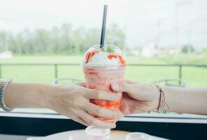 recortado Disparo ver de mujer manos participación un taza de hielo fresa Leche agitar. foto