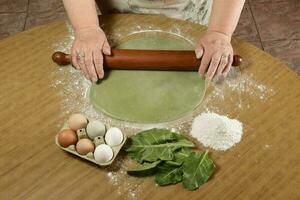 Grandma's hands kneading, dough for green noodles. photo