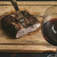 asado carne de vaca costillas con un vaso de rojo vino presentado en el mesa, tradicional argentino cocina, asado parilla, Patagonia, argentina. foto