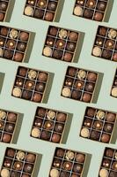 Pattern with box with chocolate craft candies with nuts inside on green background top view, flat lay photo