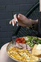 A plate with an omelette with turkey and vegetables. Female hands with a fork photo