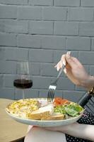 A plate with an omelette with turkey and vegetables and a glass of wine. Female hands with a fork photo