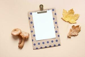 Empty paper with mushrooms and autumn leaves on beige background top view, flat lay photo