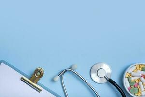 Fragment of stethoscope, tablet, pills on blue background with copy space. Healthcare and medicine concept flat lay, top view photo