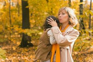 Mother soothes her crying blonde daughter. Mom holds sadness baby in her arms in autumn nature. photo