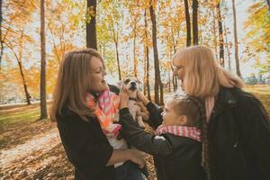 Grandmother and mother with granddaughter having fun with dog in autumn season. Generation, leisure and family concept photo