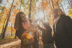 Grandmother and mother with granddaughter having fun with dog in autumn season. Generation, leisure and family concept photo