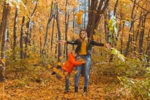 Single parent family playing with autumn leaves in park. Happy mom and son throw autumn leaves up in fall park. photo