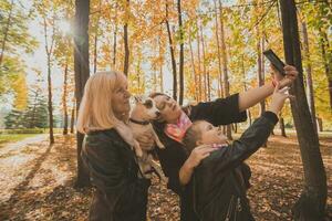 Three generations of women and dog feel fun look at camera posing for self-portrait picture together, funny excited child, mom and grandmother have fun enjoy weekend take selfie on gadget in autumn photo