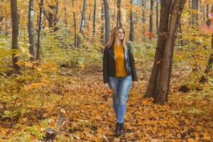 Lonely sad woman is kicking yellow leaves in autumn. Sad mood and seasonal affective disorder concept. photo