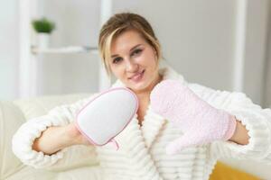 Excited joyful young woman wrapped head in towel holding dry brush shower sponge and doing spa procedure photo