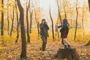 madre tomando imagen su carismático hija en retro cámara en otoño parque. aficiones y ocio concepto. foto