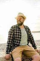 hermoso y seguro. al aire libre retrato de sonriente hombre vistiendo sombrero y Gafas de sol en playa. Días festivos viaje y verano turismo foto