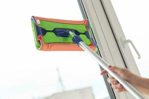 Happy woman cleaning window with sponge mop at home - housework and housekeeping concept photo