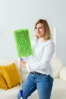 Smiling millennial woman housewife with mop for washes floor enjoys cleaning in minimalist interior. Household cleaning services and domestic work housekeeping photo