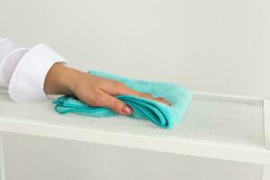 Woman wiping shelf indoors with dust rags close up. Household cleaning services and domestic work housekeeping photo