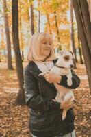 Senior smiling woman hugging her dog in autumn park. Active aging and pet concept. photo