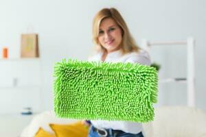 Smiling millennial woman housewife with mop for washes floor enjoys cleaning in minimalist interior. Household cleaning services and domestic work housekeeping photo