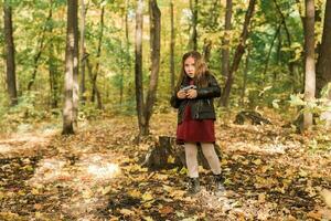 un pequeño niña tomar un foto con antiguo retro cámara en otoño naturaleza. ocio y pasatiempo concepto.