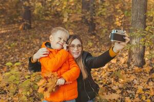 Son and mother are taking selfie on camera in autumn park. Single parent, leisure and fall season concept. photo