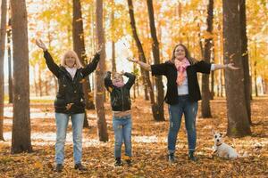 Grandmother and mother with granddaughter throw up fall leaves in autumn park and having fun. Generation, leisure and family concept. photo