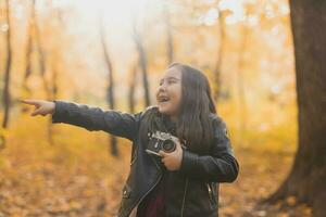 niño niña utilizando un Anticuado cámara en otoño naturaleza. fotógrafo, otoño temporada y ocio concepto. foto