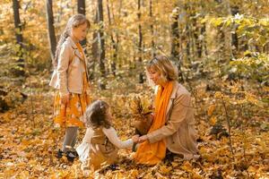 Young mother with her little daughters in an autumn park. Fall season, parenting and children concept. photo