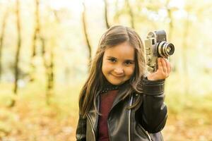 pequeño niña con foto con antiguo retro cámara en otoño naturaleza. ocio y pasatiempo concepto.