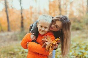 Mother hugging her child during walk in autumn park. Fall season and single parent concept. photo