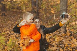 Son and mother are taking selfie on camera in autumn park. Single parent, leisure and fall season concept. photo