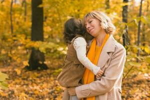 Young mother with her little daughter in an autumn park. Fall season, parenting and children concept. photo