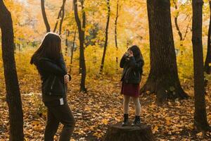 Child girl photographer takes pictures of a mother in the park in autumn. Hobbies, photo art and leisure concept.