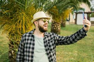 Man taking selfie portrait over palm tree background - Happy millennial guy enjoying summer holidays in city - Youth and technologies photo