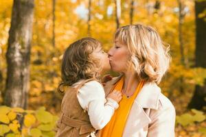 Woman with kid girl outdoors in fall. Child kissing mom. Mothers day holiday and autumn concept. photo