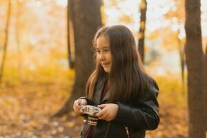 A little girl take a photo with old retro camera in autumn nature. Leisure and hobby concept.