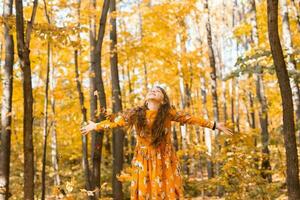 Child girl throwing fall leaves on autumn nature - fun, leisure and childhood concept photo