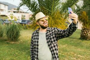 Man taking selfie portrait over palm tree background - Happy millennial guy enjoying summer holidays in city - Youth and technologies photo