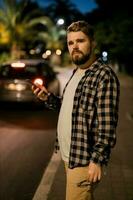 Man waits taxi by using transportation app on night street. Technologies and city concept photo