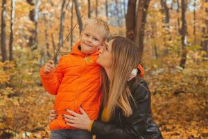 Mother hugging her child during walk in autumn park. Fall season and single parent concept. photo