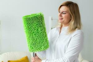 Smiling millennial woman housewife with mop for washes floor enjoys cleaning in minimalist interior. Household cleaning services and domestic work housekeeping photo