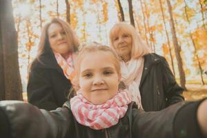 Tres generaciones de mujer y perro sensación divertido Mira a cámara posando para Auto retrato imagen juntos, gracioso emocionado niño, mamá y abuela tener divertido disfrutar fin de semana tomar selfie en artilugio en otoño foto