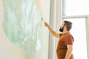Man smoothes wall surface with a wall grinder. Male grind a white plaster wall - renovation and redecoration concept. Copy space and empty space for text photo